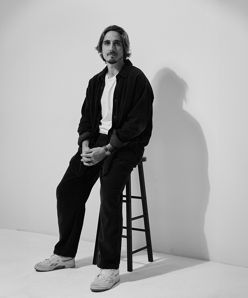 Matthew Riley sat on stool infront of grey background at SHED london photography studio and desk space