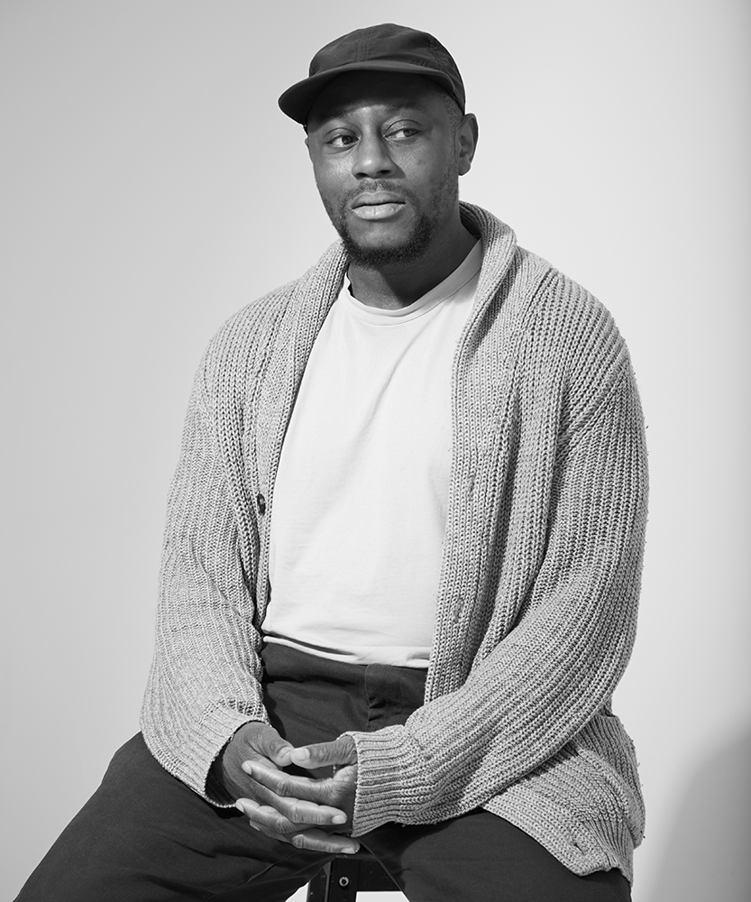 David Nwokedi sat on a stool infront of a grey background at SHED desk space in haggerston