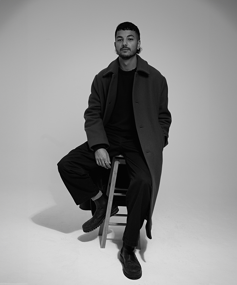 Jamie Seechurn sat on a stool in front of a grey background at SHED desk space in haggerston